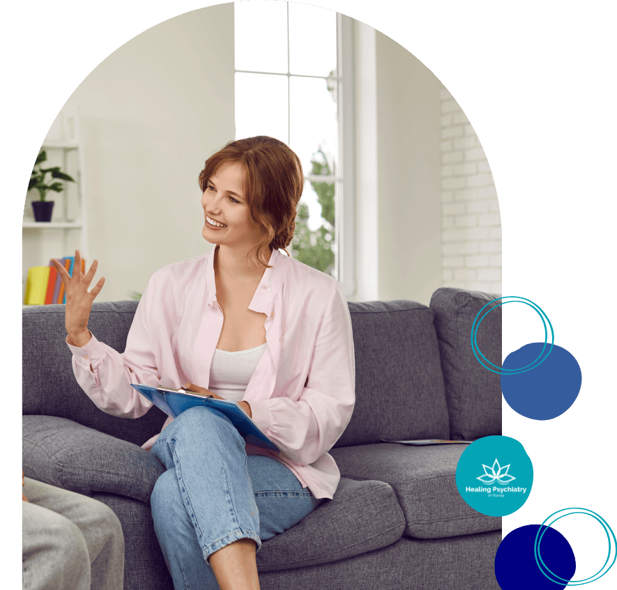A welcoming therapist with short hair is seated comfortably on a gray sofa, clipboard in hand, engaging in a discussion, exemplifying the attentive care provided by Lake Mary Psychiatric Services.