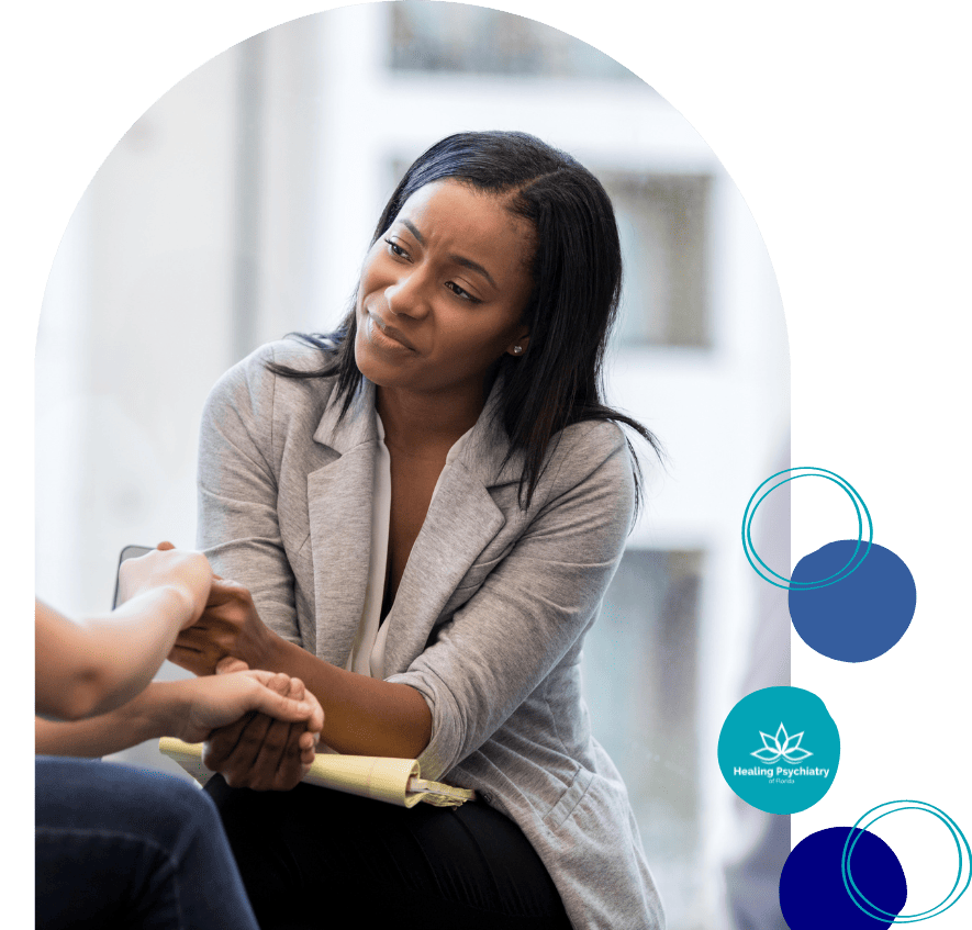 A compassionate healthcare professional from Longwood Psychiatric Services provides comfort and support to a patient. The professional is attentively listening and holding the patient's hand, symbolizing the personalized and empathetic care provided at Longwood Psychiatric Services. The setting appears calm and supportive, with the logo of Healing Psychiatry suggesting a focus on recovery and mental well-being.